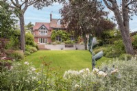 Vue sur pelouse à la maison avec pièce d'eau et terrasse de parterre pastel avec sculpture de canard sauvage