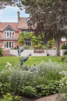 Vue sur pelouse à la maison avec pièce d'eau et terrasse de parterre pastel avec sculpture de canard sauvage