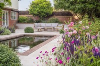 Coin salon sur terrasse en grès avec piscine rectangulaire bordée de briques et parterre de roses David Austin,