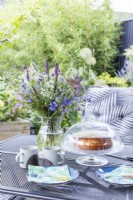 Table dans le jardin avec bouquet de fleurs, boissons chaudes et gâteau fraîchement sorti du four