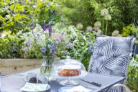 Table de jardin avec bouquet de fleurs, boissons chaudes, assiettes et gâteau fraîchement sorti du four