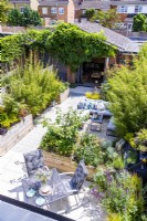 Jardin de banlieue avec coins salons, parterres de fleurs surélevés en bois et parterres de fleurs en bambou avec maison d'été couverte de glycines