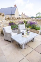 Table et chaises de jardin en osier sur patio devant un parterre de fleurs surélevé