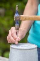Femme utilisant un marteau et un clou pour faire des trous de drainage au fond des seaux métalliques