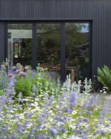 L'extension moderne vue du fond du jardin à travers les parterres fleuris et la pelouse du pré.