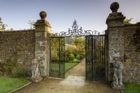 Une vue sur le jardin clos à travers des portes ornementales flanquées de lions en pierre à Parham House en septembre