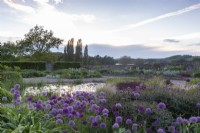 Vue du lever du soleil sur le gravier - alliums et parterres de fleurs en plantation mixte et petit étang