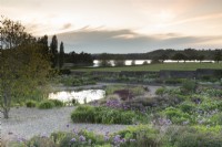 Vue du lever du soleil sur le jardin de gravier en direction du lac Blagdon - diverses variétés d'alliums et parterres de fleurs mixtes et petit étang