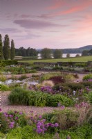 Vue du lever du soleil sur le jardin de gravier en direction du lac Blagdon - alliums, graminées ornementales, Lysimachia ciliata 'Firecracker' et parterres de fleurs mixtes et petit étang