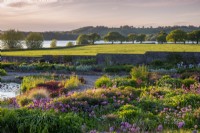 Vue du lever du soleil sur le jardin de gravier en direction du lac Blagdon - alliums et parterres de fleurs mixtes et petit étang