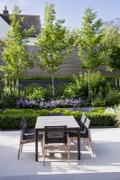 Table à manger et chaises sur patio pavé pâle dans un jardin moderne