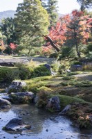 Ruisseau dans le jardin avec rochers et vue sur les arbres aux couleurs d'automne et sur les collines à l'extérieur du jardin
