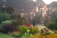 Dahlias rouges « Bishop of Llandaff », « Babylon Red » et Rudbeckia dans un parterre de fleurs aux jardins de Waterperry au lever du soleil. 