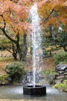 Fontaine dans un petit bassin, considérée comme la plus ancienne fontaine du Japon, datant du 19e siècle et alimentée par l'étang Kasumigaike. Arbres aux couleurs d'automne derrière. 