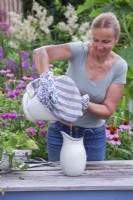 Faire de l'engrais et de l'insecticide à base d'ortie. Femme filtrant le mélange d'eau et d'orties à travers le torchon dans une cruche en émail. 