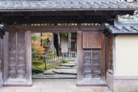 Vue sur l'entrée de la maison et du jardin avec des avis en japonais et de larges tremplins à l'intérieur de l'entrée et une balustrade basse en bambou. 