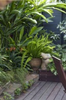 Détail d'angle d'un jardin subtropical ombragé comprenant une fougère sétaire en pot, Heliconia et Philodendron, Xanadu. et une sculpture en céramique représentant une femme nue. 