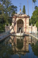 Le Cenador del Leon, Pavillon du Lion, se reflète dans une piscine entourée de balustrades métalliques et avec une sculpture d'un lion dans la piscine. Jardins du véritable palais de l'Alcazar, Séville. Espagne. Septembre. 