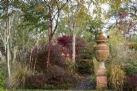 Urne en terre cuite entourée d'arbustes, de graminées ornementales et d'arbres dont Prunus serrula et bouleaux à tige blanche en novembre 