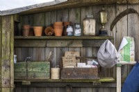 Des boîtes anciennes en bois avec des livres de jardinage vintage, des paquets de graines et des pots en argile, de la ficelle de jardin et des bocaux se trouvent sur des étagères dans un hangar en bois 
