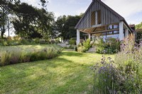Jardin champêtre en juillet avec parterres de plantes herbacées vivaces autour d'une extension de maison contemporaine 