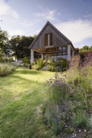 Jardin champêtre en juillet avec parterres de plantes herbacées vivaces autour d'une extension de maison contemporaine 