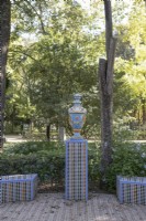 Une urne colorée et vitrée, posée sur un socle, avec des bancs bas et incurvés carrelés, décorés dans le style islamique mudéjar. divers arbustes et arbres sont en arrière-plan. Parque de Maria Luisa, Séville, Espagne. Septembre 