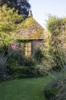 Un pavillon d'été en brique avec un toit de tuiles situé au milieu de plantations comprenant du stipa dans The Circles at The Manor, Little Compton. 