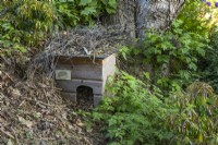 Maison de hérisson en bois camouflée avec des brindilles dans un jardin boisé 