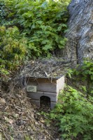Maison de hérisson en bois camouflée avec des brindilles dans un jardin boisé 