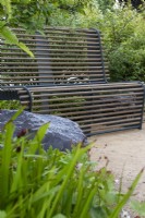Un siège à structure métallique avec des tiges en bois placées parmi les plantations - Cancer Research UK Legacy Garden - designer Paul Hervey-Brookes - RHS Hampton court Flower Palace Garden Festival 2023. 