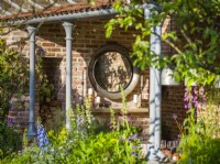 Miroir circulaire sur mur de briques dans une salle à manger extérieure. The Savills Garden, Designer : Mark Gregory, RHS Chelsea Flower Show 2023, mai, printemps, été 
