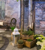 Exposition d'herbes et d'hortensias en pots et lanterne devant la maison en pierre de cour italienne contemporaine. Un canal d'eau qui coule sur la surface de gravier. 