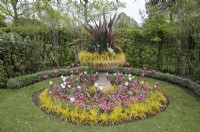 Urne avec cordyline et graminées ornementales debout dans un parterre de fleurs circulaire avec un arrangement de tulipes roses et blanches et de couverture de sol bellis, Avenue Gardens, The Regent's Park, Londres, Royaume-Uni 